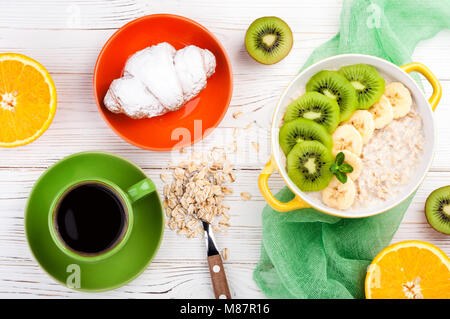 Le petit-déjeuner avec du gruau d'avoine, de croissants, de fruits et de tasse à café. Avoine avec kiwi, l'orange et la banane. Petit-déjeuner sain concept. Vue d'en haut Banque D'Images