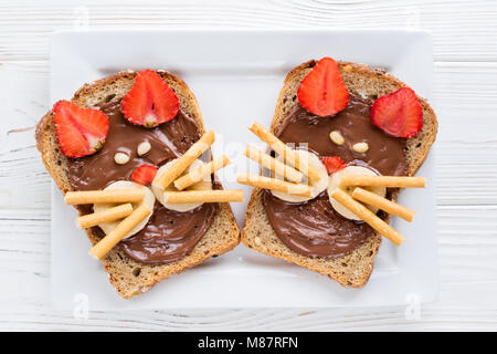 Le petit déjeuner des enfants avec des sandwichs et du lait. Funny cats face sandwiches avec berry, chocolat, banane, noix. Vue d'en haut Banque D'Images