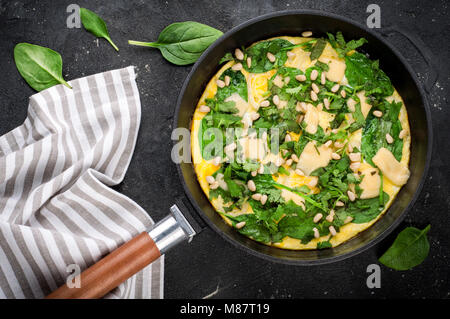 Omelette avec les oeufs, les épinards, les noix de pin et de légumes. Tortilla d'épinards dans le moule, sur fond sombre. Délicieux petit-déjeuner ou snack apéritif. Vue d'en haut Banque D'Images