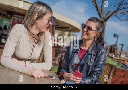 Deux belles jeunes femmes s'amuser en plein air tout en utilisant leurs smartphones, d'amitié, de bonheur et de personnes - deux smiling girls whispering g Banque D'Images