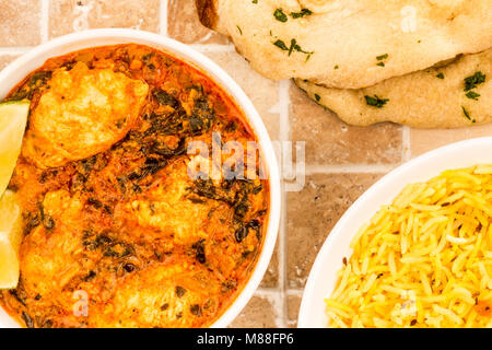 Le style indien Curry Masala Poulet Saag sur un sol carrelé Table de cuisine haut avec naan pain plat et riz pilaf Banque D'Images