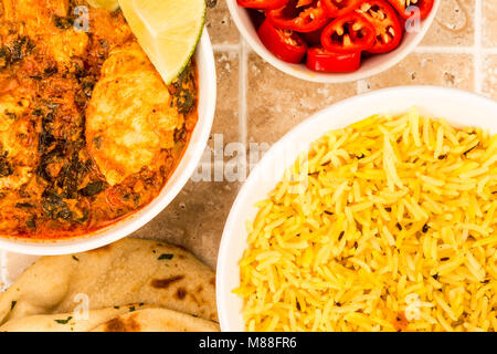 Le style indien Curry Masala Poulet Saag sur un sol carrelé Cuisine Table en pain naan piments rouges et riz pilaf Banque D'Images