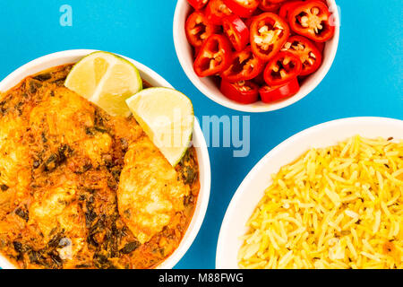 Le style indien Curry Masala Poulet Saag contre un fond bleu avec du riz pilaf, des piments et des quartiers de lime Banque D'Images