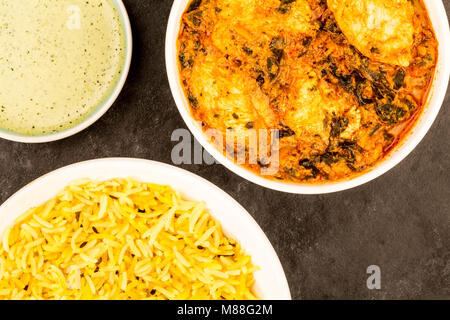 Le style indien Curry Masala Poulet Saag contre un fond noir avec le riz Pilau jaune et trempette Banque D'Images