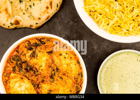 Le style indien Curry Masala Poulet Saag contre un fond noir avec le riz Pilau jaune pain plat Naan et une sauce Banque D'Images