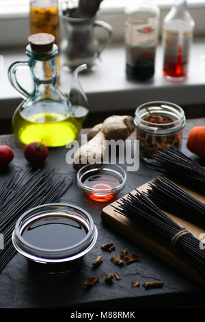 Vermicelles de riz noir et de légumes sur la table, les bouteilles de vinaigre sur le rebord. Verticale de la cuisine asiatique Banque D'Images