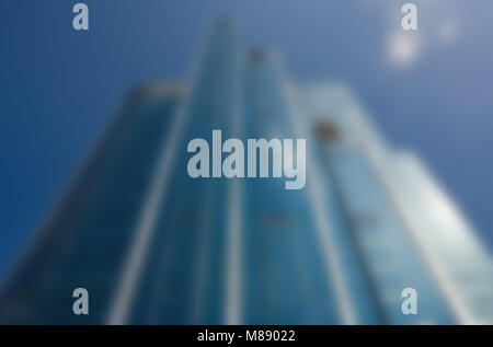 Image floue low angle de la façade en verre d'un gratte-ciel moderne contre un ciel bleu dans le quartier commerçant d'une ville Banque D'Images