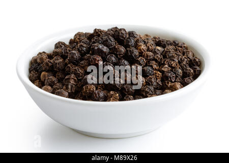 Grains de poivre noir dans le bol en céramique blanc isolé sur blanc. Banque D'Images