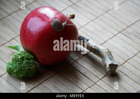 Assis sur l'escargot pomme rouge et de tronc d'arbre et rendez-vous au vert le brocoli, toile de bambou en bois, close-up animal fond. Banque D'Images