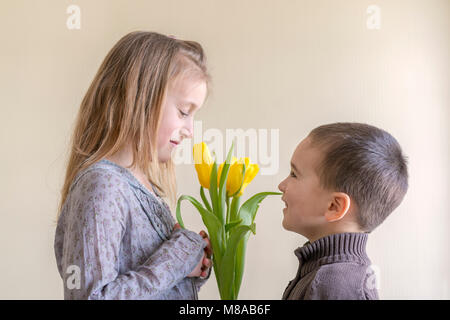 Le petit homme donne à la jeune fille un bouquet de fleurs. Le petit garçon donne un bouquet de tulipes jaunes Banque D'Images
