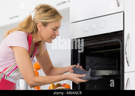 Jolie blonde woman putting tart dans le four pour la cuisson Banque D'Images