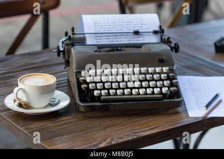 Offres et demandes d'écriture et de concept. Typeweriter rétro avec du papier, des crayons et une tasse de cappuccino sur table en bois. Banque D'Images