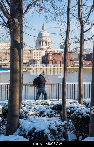 Un homme qui marche le long du sentier sur la thames path ou banque de la Tamise dans le centre de londres, dans l'hiver neige avec la cathédrale St Paul. Banque D'Images