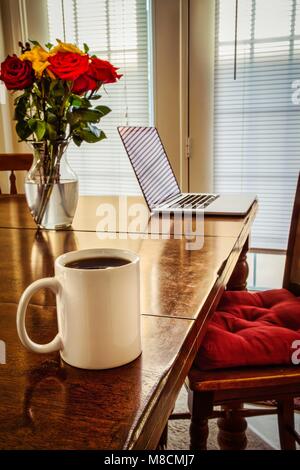 Une tasse à café, un ordinateur, floweres, tous assis sur une table. Banque D'Images