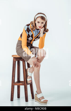 Beau style retro girl sitting on wooden chair and looking at camera on white Banque D'Images