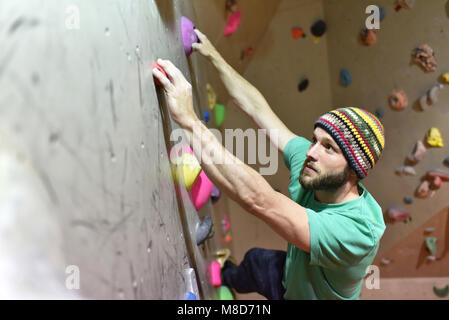 Bouldering grimpeur dans une salle de sport - la tenue à la poignée d'un mur en pierre artificielle Banque D'Images