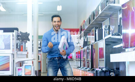 Dans le magasin d'Électronique Jeune homme nouvellement acheté tablette ordinateur détient et heureusement les sauts avec elle. Store est moderne, lumineux et dispose de toutes les dernières plat Banque D'Images