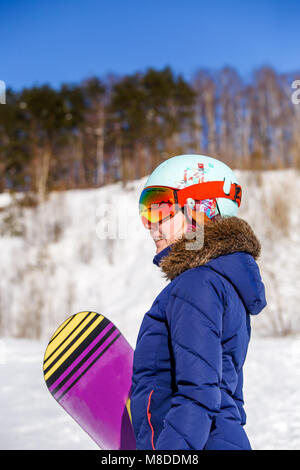 Vue latérale du sporty woman wearing helmet with snowboard looking at camera Banque D'Images