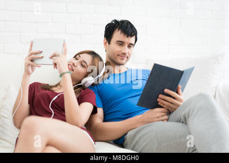 Couple sur le canapé dans leur salle de séjour à la maison. Écouter de la musique et lire un livre. Banque D'Images
