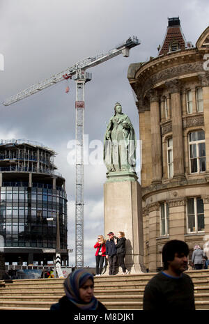 Les touristes posent sous une statue de la reine Victoria à Birmingham's Square Victoria avec nouveau bâtiment travaux en cours dans l'arrière-plan. Banque D'Images