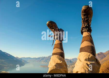 Des chaussures de randonnée et les jambes en l'air sur la chaîne de montagnes des Alpes et du Lac Majeur au Tessin, Suisse Banque D'Images