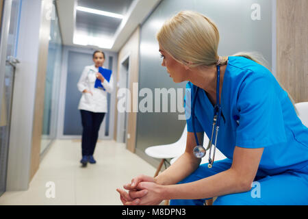 Assis dans le couloir de l'hôpital Médecin-chef, se penchant en avant, médecin à marcher le long couloir Banque D'Images