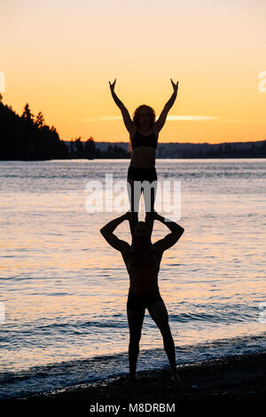 Couple practicing yoga on beach at sunset Banque D'Images