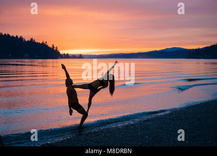 Couple practicing yoga on beach at sunset Banque D'Images