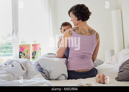 Assis sur le lit de la mère, holding baby girl, vue arrière Banque D'Images