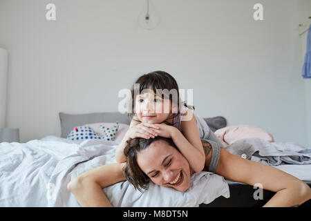Mother and Daughter lying on bed, daughter lying on mother's back Banque D'Images