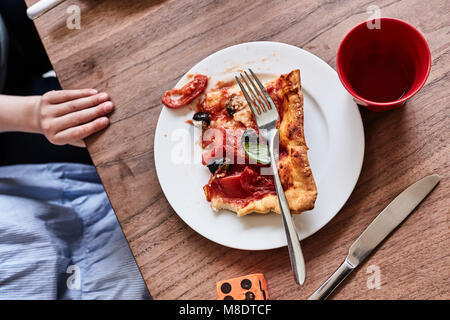 Tranche de pizza sur plaque blanche, la main de l'enfant sur la table, mid section, elevated view Banque D'Images