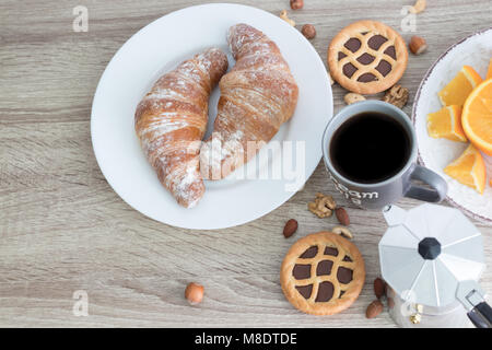 Petit déjeuner européen avec 2 gros croissants sur la plaque blanche tasse à café, et les tranches orange juteuse avec des gâteaux et des écrous sur fond de bois. Vue d'en haut. S COPIE Banque D'Images