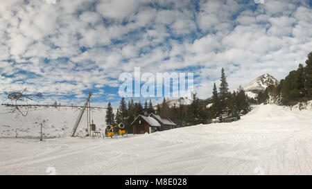 Piste rouge vide sur Strbske Pleso, Solisko ski aux beaux jours de printemps avec des nuages dans l'arrière-plan et en premier plan de neige damée. Banque D'Images