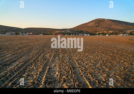 Des pistes de pneus de voiture sur le sable de grande plage vide de l'océan contre les hautes collines du camp et ciel bleu clair en soirée d'été à faible angle de vue Banque D'Images