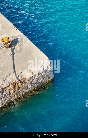 Mouillage jaune bitt avec corde sur quai en béton gris à l'eau de mer bleue avec de petites vagues sous la lumière du soleil vive le jour d'été Banque D'Images