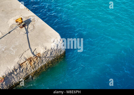 Mouillage jaune bitt avec corde sur quai en béton gris à l'eau de mer bleue avec de petites vagues sous la lumière du soleil vive le jour d'été Banque D'Images