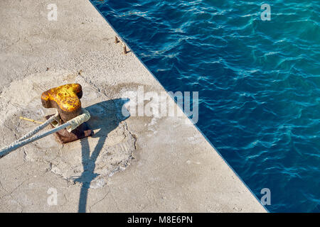 Mouillage jaune bitt avec corde sur quai en béton gris à l'eau de mer bleue avec de petites vagues sous la lumière du soleil vive le jour d'été Banque D'Images