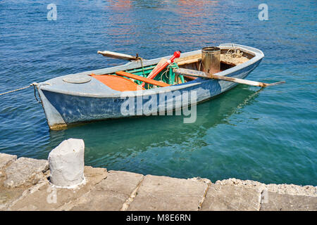 Bateau avec des oars amarrés à la jetée avec des cordes sur l'eau de mer bleue reflétant la lumière du soleil la journée d'été Banque D'Images