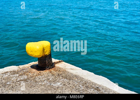 Mouillage jaune bitt sur une jetée en béton gris à l'eau de mer bleue avec de petites vagues sous la lumière du soleil le jour d'été Banque D'Images