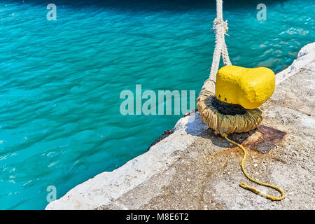 Mouillage jaune bitt avec corde sur quai en béton gris à l'eau de mer bleue avec de petites vagues sous la lumière du soleil vive le jour d'été Banque D'Images