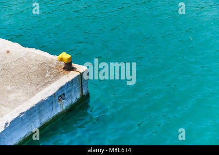 Mouillage jaune bitt sur une jetée en béton gris à l'eau de mer bleue avec de petites vagues sous la lumière du soleil le jour d'été Banque D'Images