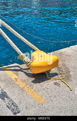 Mouillage jaune bitt avec corde sur quai en béton gris à l'eau de mer bleue avec de petites vagues sous la lumière du soleil vive le jour d'été Banque D'Images