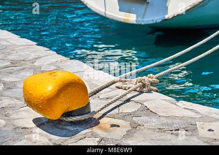 Mouillage jaune bitt avec corde sur quai en béton gris à l'eau de mer bleue avec de petites vagues sous la lumière du soleil vive le jour d'été Banque D'Images