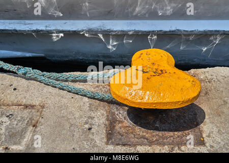 Mouillage jaune bitt avec corde sur quai en béton gris à l'eau de mer bleue avec de petites vagues sous la lumière du soleil vive le jour d'été Banque D'Images