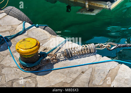 Mouillage jaune bitt avec corde sur quai en béton gris à l'eau de mer bleue avec de petites vagues sous la lumière du soleil vive le jour d'été Banque D'Images