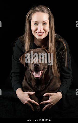 La jeune femme serrant chien labrador noir toile noire prise contre au studio Banque D'Images