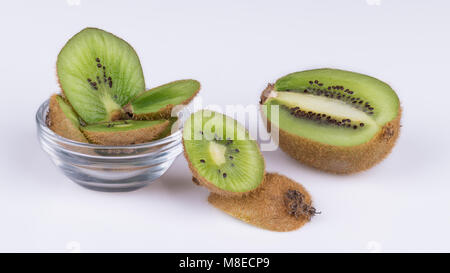 Tranches de morceaux de kiwis avec la peau brune. L'Actinidia deliciosa. Vert décoratif tranches de kiwifruits aigre-doux dans un bol en verre et sur fond blanc. Banque D'Images