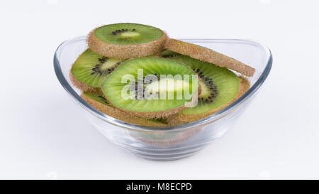 Tranches de kiwi vert dans la cuvette en verre. Les kiwis floue. L'Actinidia deliciosa. Close-up de tas de tranches de fruits tropicaux avec la peau brune. Arrière-plan blanc. Banque D'Images