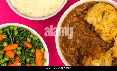 Goulasch de Bœuf britannique traditionnel, avec des boulettes contre un fond rose avec un bol de purée de pommes de terre et légumes Banque D'Images