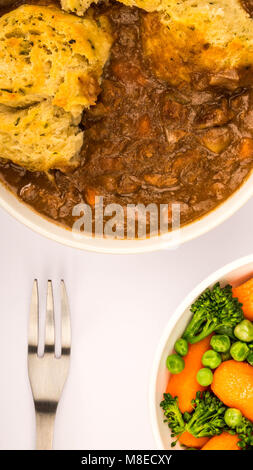 Goulasch de Bœuf britannique traditionnel, avec des boulettes contre un fond bleu pâle et un bol de légumes Banque D'Images
